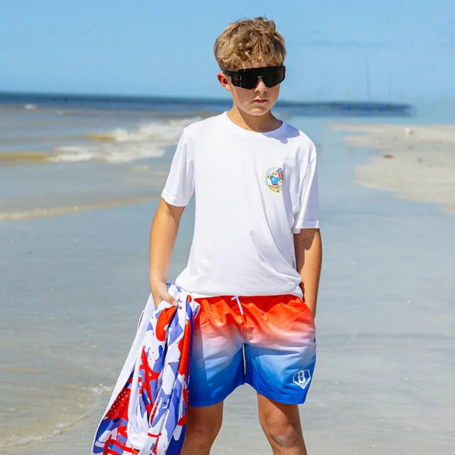 Boy at the beach with white shirt and colorful shorts.