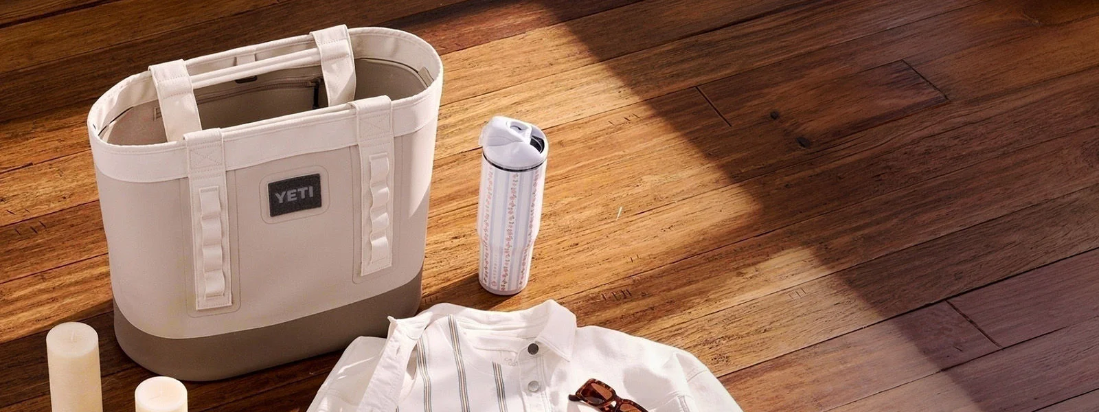 YETI bag next to tumbler, shirt, sunglasses and candles on wooden floor.