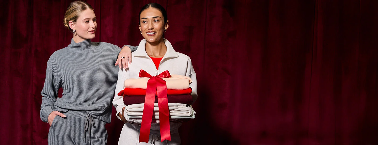 Two women holding a pile of hoodies. 
