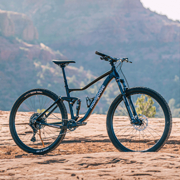 A child riding in the dirt on their blue kids mountain bike made by Mongoose.