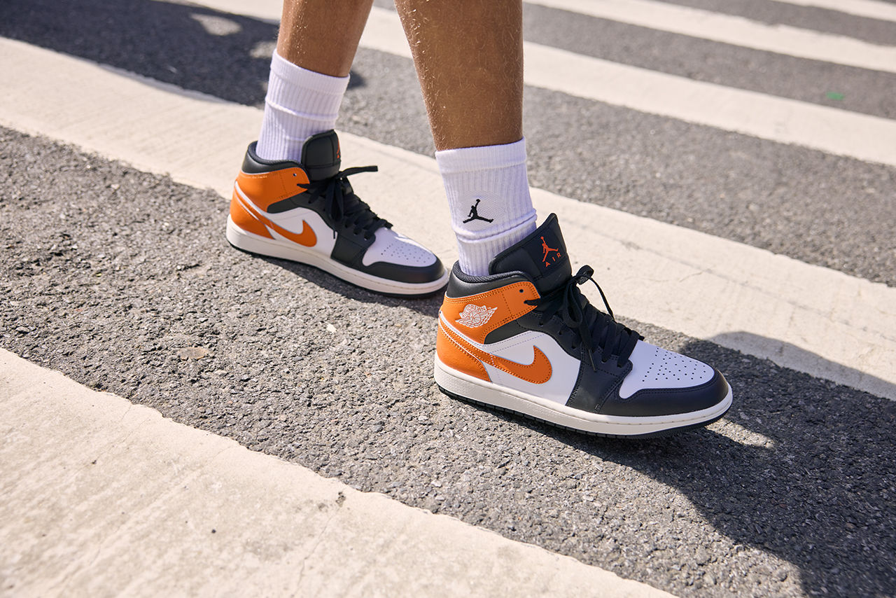 Orange, white and black Nike Air Jordan sneakers on pavement