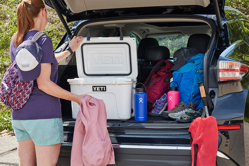 woman opening a Yeti cooler in the back of an SUV with camping gear scattered around the trunk
