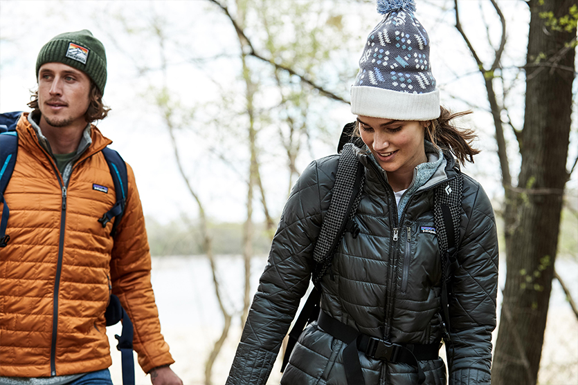 man and woman hiking throught he woods wearing cold weather clothes and backpacks