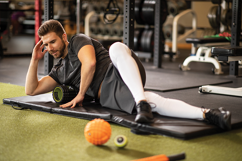 A man using a foam roller on a gym mat.