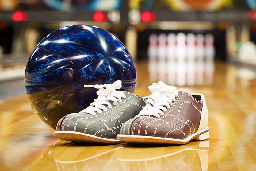 picture of bowling shoes and a bowling ball on a bowling kane with pins blurred out in the background