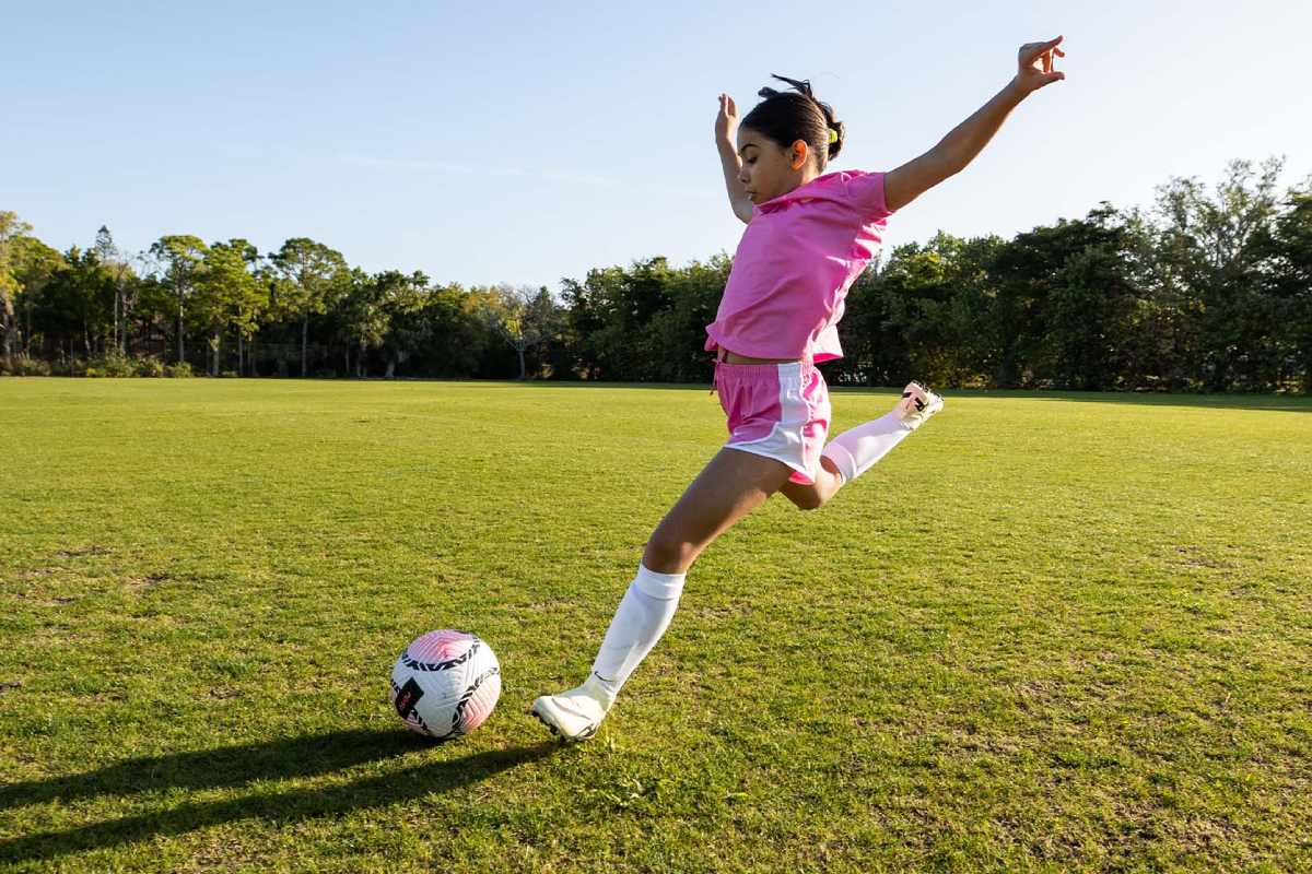 girl kicking soccer ball on field