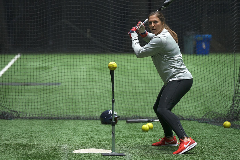 image featuring a woman ready to hit a softball on a batting cage