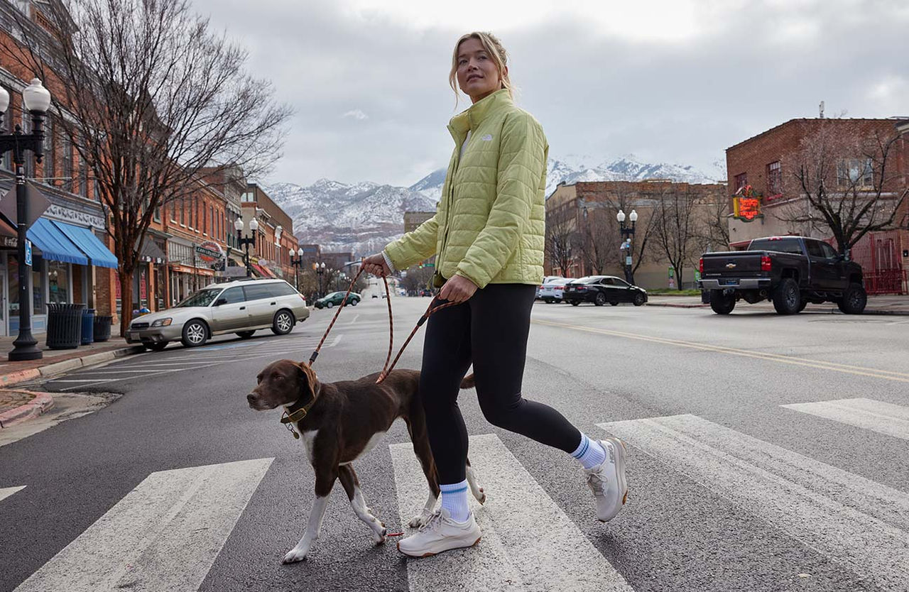 girl walking dog in coat with mountain scenery behind