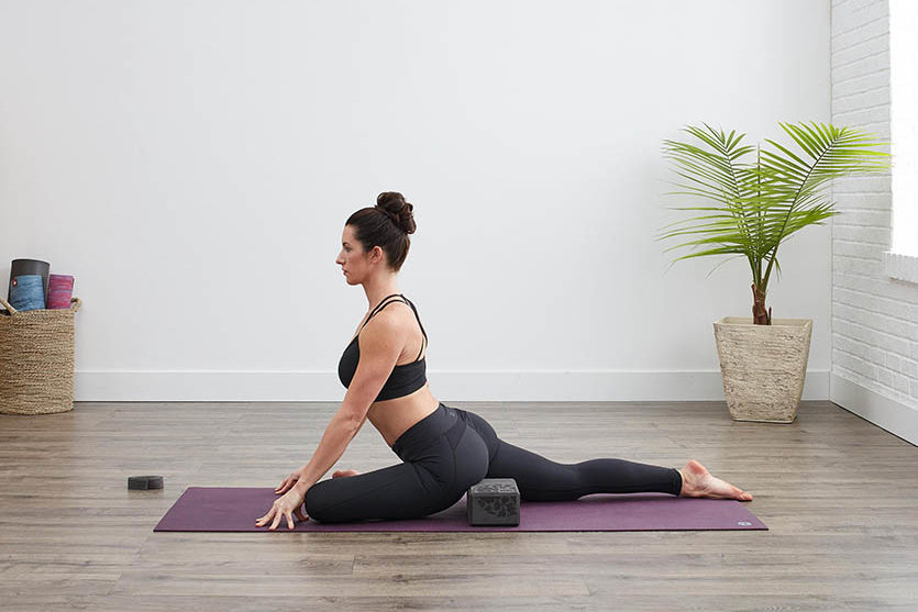 Women practicing half pigeon pose with yoga block